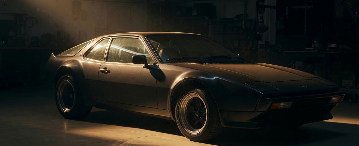 Coupé sport allemand des années 1980 à profil en coin, éclairé par un faisceau rasant dans un atelier sombre